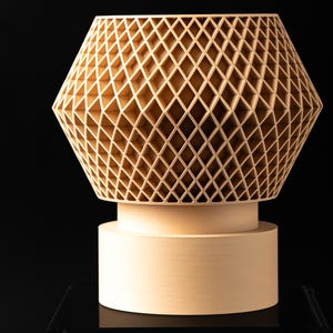 May include: A light beige vase featuring a complex, three-dimensional lattice structure with a repeating diamond pattern. The upper section is wide and geometric, while the base is a solid, smooth, cylindrical pedestal.