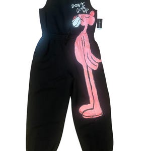 May include: Black jumpsuit featuring a pink panther graphic on the side. The sleeveless jumpsuit has a drawstring waist and the words "DON'T GIVE UP" above the panther. The jumpsuit is made of a soft material.