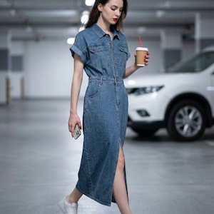 May include: A medium-wash blue denim midi dress featuring a collared neckline, short cuffed sleeves, a button-down front, two chest pockets, and a front slit. The dress is paired with white low-top sneakers, a smartphone, and a disposable coffee cup.