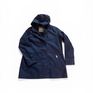 May include: A navy blue hooded jacket with a button-up front and two front pockets. The jacket has a drawstring waist and a small white tag on the sleeve. The jacket is made of a water-resistant material.