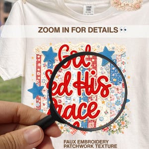 May include: A white t-shirt with a patriotic design. The design features the words "God Ed His Grace" in red script, blue stars, and a patchwork pattern. The text "Zoom in for details" is also visible.