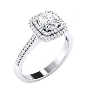 Może przedstawiać: Srebrny pierścionek zaręczynowy z dużą, okrągłą, przezroczystą kamieniem centralnym. Kamień centralny otoczony jest podwójną aureolą z mniejszych, przezroczystych kamieni. Dodatkowe małe kamienie osadzone są wzdłuż obrączki pierścionka.