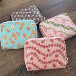 May include: Four small, zippered wallets with floral patterns. One is light blue with orange flowers, another is pink with pink flowers, a third is pink with green leaves and pink flowers, and the last is brown with white shapes.