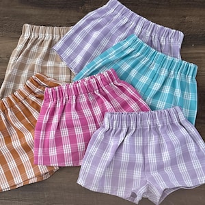 May include: A collection of plaid shorts in various colors, including brown, pink, purple, and teal. The shorts have an elastic waistband and a relaxed fit, perfect for casual wear. The plaid pattern is a classic design.