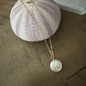 May include: A gold chain necklace with a white, round, iridescent pendant. The pendant is made of a natural material, possibly mother of pearl.