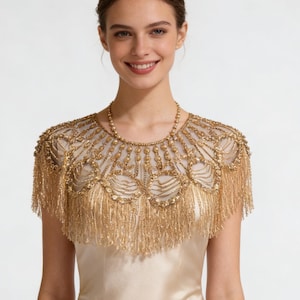 Peut inclure: Un capeline dorée à franges, portée sur une robe en satin. La capeline présente des perles complexes et une frange délicate. La robe est de couleur champagne clair.