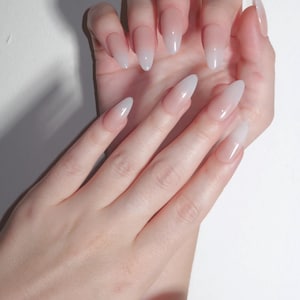 Pode incluir: Duas mãos com unhas artificiais longas em forma de amêndoa. As unhas apresentam um efeito gradiente, passando de um rosa pálido na base a um branco brilhante nas pontas. As unhas são brilhantes e bem cuidadas.