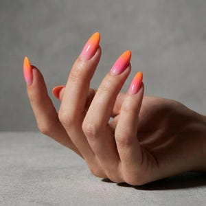 Puede incluir: Una mano con uñas largas en forma de almendra. Las uñas presentan un diseño degradado, que transiciona de un naranja brillante en las puntas a un rosa suave en la base. Las uñas son brillantes y están bien cuidadas, creando un look vibrante y elegante.