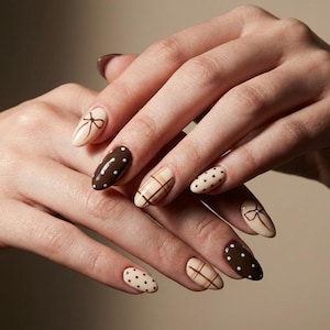 Op de afbeelding: Amandelvormige nagels met diverse ontwerpen. Sommige nagels zijn lichtbeige geverfd met een bruin strikpatroon. Andere hebben een donkerbruine basis met witte stippen, en sommige hebben een ruitpatroon.