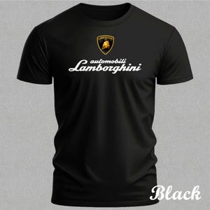 以下が含まれることがあります： ランボルギーニのロゴと白文字が入った黒いTシャツ。ロゴは黒い雄牛が入った金の盾です。「automobili Lamborghini」の文字は筆記体で書かれています。「Black」の文字は右下に筆記体で書かれています。