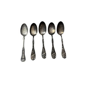 May include: Five antique silver spoons on a white background. The spoons have decorative floral and scrollwork patterns on the handles. The spoons are tarnished, showing signs of age and use.