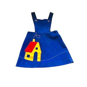 Puede incluir: Vestido peto de pana azul con aplique de casa. La casa tiene tejado rojo y paredes amarillas. El vestido tiene tirantes ajustables y cierre de botón. Estilo vintage.