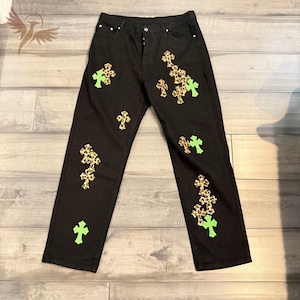 Puede incluir: Vaqueros negros con múltiples diseños de cruces. Las cruces son una mezcla de estampado de leopardo y verde neón. Los vaqueros tienen un diseño clásico de cinco bolsillos y cierre de botón y cremallera.