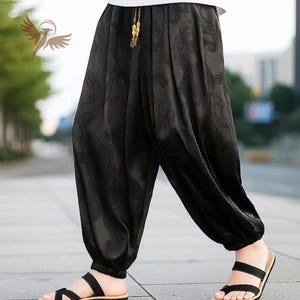 May include: Black, loose-fitting trousers with a subtle dragon pattern. The trousers have a drawstring waist and are gathered at the ankles. The person is wearing black sandals with the trousers.