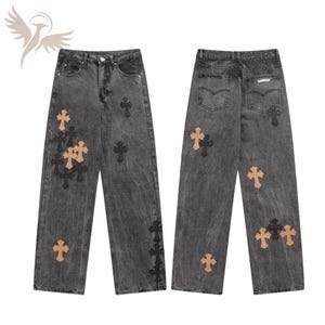 Peut inclure: Un jean en denim gris délavé avec une coupe large. Le jean présente de multiples applications de croix en noir et beige. L'avant et l'arrière du jean sont visibles, mettant en valeur les détails du design.