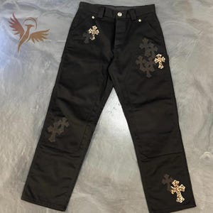 Może przedstawiać: Czarne spodnie z wieloma wzorami krzyży, niektóre z nadrukiem w cętki. Spodnie mają zapięcie na guzik i zamek błyskawiczny, z kieszeniami z przodu i z tyłu. Materiał wydaje się wytrzymały.