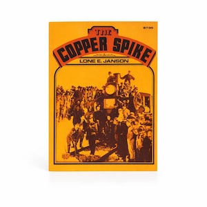 May include: A white ceramic mug with a black handle and the text "But First, Coffee" in a bold, black font. The mug is set against a blurred background, suggesting a cozy setting.