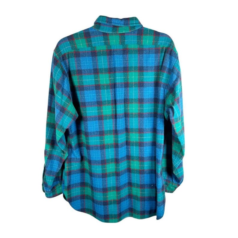 May include: A long-sleeved, button-down flannel shirt in a plaid pattern. The shirt features a color scheme of teal, blue, and red. The collar and cuffs are visible, and the shirt is made of a soft, woven fabric.