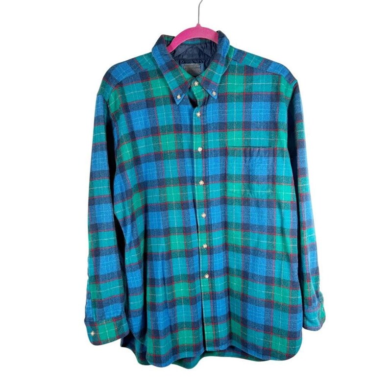 May include: A button-down plaid shirt in shades of blue, green, and red, hanging on a pink hanger. The shirt has a chest pocket and a button-down collar. The fabric appears to be a soft flannel.