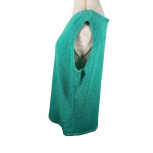 Puede incluir: Una blusa sin mangas de color verde azulado, con tejido de punto texturizado. La blusa tiene un cuello redondo y un corte holgado. La prenda se muestra en un maniqu&iacute;, mostrando el perfil lateral y el dise&ntilde;o de la sisa abierta.
