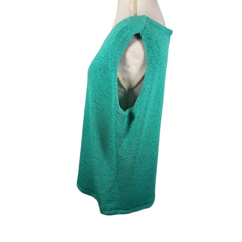 Puede incluir: Una blusa sin mangas de color verde azulado, con tejido de punto texturizado. La blusa tiene un cuello redondo y un corte holgado. La prenda se muestra en un maniqu&iacute;, mostrando el perfil lateral y el dise&ntilde;o de la sisa abierta.
