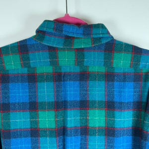 May include: A close-up of a blue, green, and red plaid flannel shirt. The shirt is hanging on a pink hanger. The plaid pattern is made up of intersecting lines of blue, green, and red, creating a classic look.