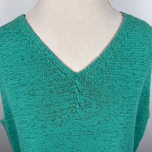 Puede incluir: Una camiseta sin mangas de punto verde esmeralda con cuello en V profundo. La tela de punto tiene una textura sutil y un ligero aspecto moteado. El escote est&aacute; reforzado con una costura en contraste, a&ntilde;adiendo un toque de detalle.