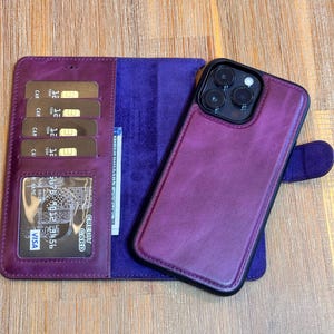 Może przedstawiać: Śliwkowy skórzany futerał na telefon z pasującym portfelem. Portfel ma przegródki na karty i przezroczyste okienko na dowód. Czarny telefon z trzema aparatami znajduje się w etui. Portfel jest otwarty, ukazując karty i gotówkę.