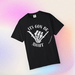 May include: A black short-sleeve t-shirt featuring a white graphic of a skeleton hand making a shaka sign. The text "ITS GON BE" is printed above the hand, and "AIGHT" is printed below it in a white serif font. The brand tag is visible.