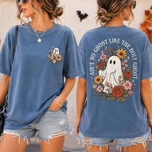 May include: A blue short-sleeve t-shirt featuring a small ghost and flower graphic on the front left chest and a large back graphic of a ghost surrounded by colorful flowers with the text AIN'T NO GHOST LIKE THE HOLY GHOST.