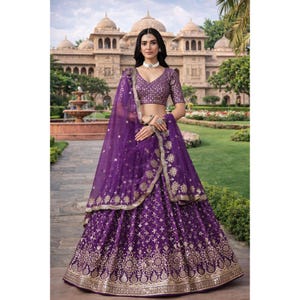 Könnte beinhalten: Ein lebendiges lila Lehenga mit aufwendiger goldener Stickerei. Das Ensemble umfasst eine passende Bluse und einen transparenten Dupatta. Der Rock hat ein detailliertes Muster, geeignet für besondere Anlässe.