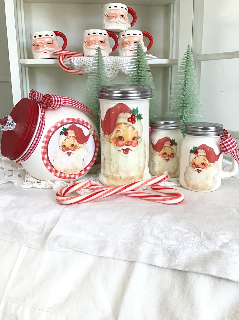 May include: White ceramic Santa Claus themed sugar and spice jars with red and white gingham ribbon and candy canes. The jars have red lids and are decorated with a Santa Claus image.