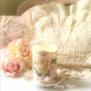 May include: A white pillar candle with a floral design and pink ribbon. The candle is decorated with rhinestones and sits on a small white saucer with a floral design. The candle is surrounded by pink and white roses.