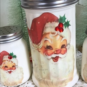 May include: Set of three white ceramic Christmas sugar shakers with red and green Santa Claus designs and red rhinestone accents.