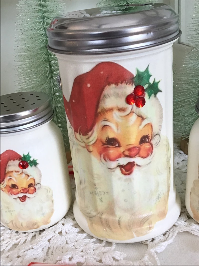 May include: Set of three white ceramic Christmas sugar shakers with red and green Santa Claus designs and red rhinestone accents.