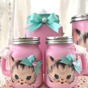 Puede incluir: Conjunto de tres tarros de cristal rosa con un dise&ntilde;o de gatito. Los tarros tienen una cinta turquesa y un adorno de strass. Los tarros son perfectos para guardar objetos peque&ntilde;os o para usar como elemento decorativo.