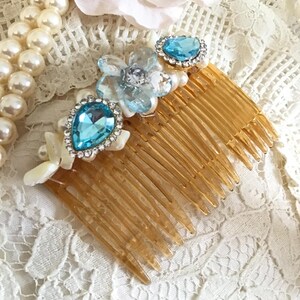 May include: A brown plastic hair comb with a decorative design featuring blue and white flowers and rhinestones.