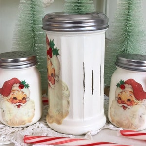 May include: Three white ceramic salt and pepper shakers with vintage Santa Claus illustrations and red holly accents. The shakers have silver lids and are sitting on a white doily with candy canes.