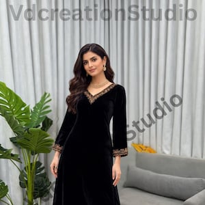 Könnte beinhalten: Ein schwarzer Palazzo-Hosenanzug aus Samt mit goldener Stickerei. Die langärmlige Tunika hat einen V-Ausschnitt und goldene Verzierungen. Die Palazzo-Hose hat eine passende goldene Stickerei am Saum. Das Outfit wird mit Goldschmuck getragen.