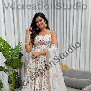 May include: White floral print dress with spaghetti straps and a matching sheer scarf. The dress features a colorful floral pattern with red, yellow, and blue accents. The dress is floor-length and has a flowing silhouette, perfect for special occasions.