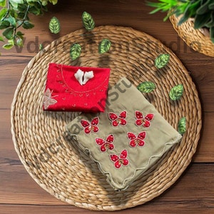 May include: A red embroidered pouch and a light green cloth with red butterfly designs rest on a woven mat. Decorative green leaf accents are scattered around the items, suggesting a nature-inspired theme.