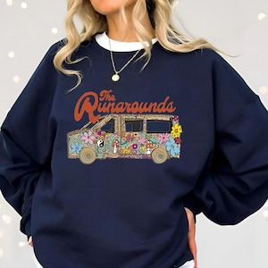 May include: Navy blue sweatshirt featuring a colorful graphic of a van with floral and mushroom designs. The text "The Runarounds" is arched above the van. The van has a retro, psychedelic vibe.