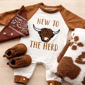 Peut inclure: Ensemble de v&ecirc;tements pour b&eacute;b&eacute; comprenant un body blanc et marron avec l'inscription "NEW TO THE HERD" et un motif de vache des Highlands. Comprend un bandana marron, des chaussures de b&eacute;b&eacute; marron et une couverture &agrave; imprim&eacute; vache.