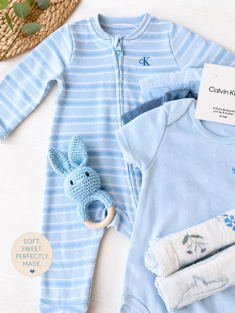 branded Calvin klein baby gift set, including Calvin Klein sleeper and 4 bodysuits. it also includes a blue baby rattle and muslin clothes. branded baby boy gift ready gift set. baby boy gift set under 50 dollars. baby shower boy gift set. baby boy essentials