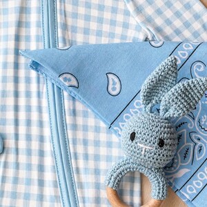 Puede incluir: Un pijama azul beb&eacute; con estampado de cuadros vichy con una bandana a juego y un sonajero de conejito de ganchillo con un anillo de madera. El pijama tiene cierre de cremallera. La bandana tiene un dise&ntilde;o de cachemira.