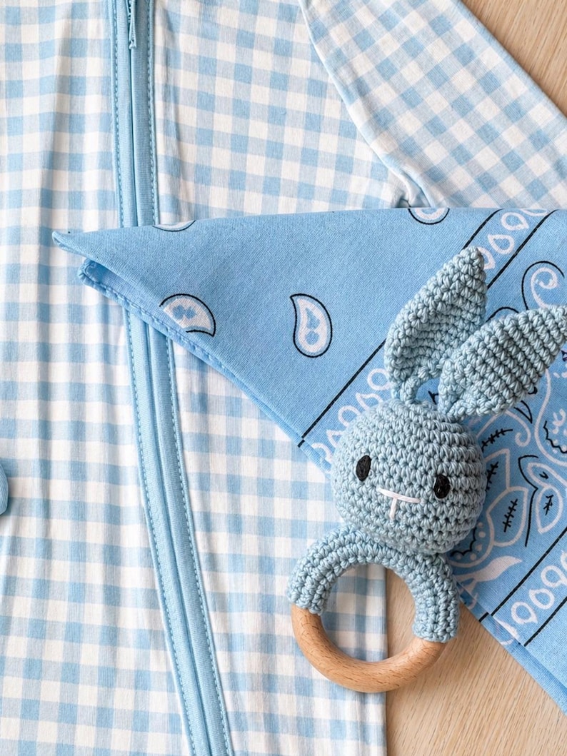 Puede incluir: Un pijama azul beb&eacute; con estampado de cuadros vichy con una bandana a juego y un sonajero de conejito de ganchillo con un anillo de madera. El pijama tiene cierre de cremallera. La bandana tiene un dise&ntilde;o de cachemira.