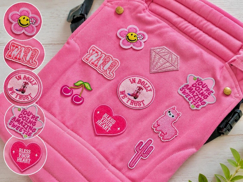 K&ouml;nnte beinhalten: Rosa Stoff mit gestickten Aufn&auml;hern verziert. Aufn&auml;her zeigen eine l&auml;chelnde Blume, das Wort "Y'all", eine Raute, Kirschen, ein Herz mit "Bless Your Heart", einen Kaktus und ein Alpaka. Der Satz "In Bolly We Trust" ist ebenfalls sichtbar.