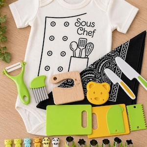 Puede incluir: Un body blanco para beb&eacute; con un gr&aacute;fico de "Sous Chef", junto con una variedad de utensilios de cocina, incluyendo un pelador, cuchillos, tablas de cortar y pinchos para alimentos. El conjunto incluye cortadores de galletas con forma de oso y una bandana negra.