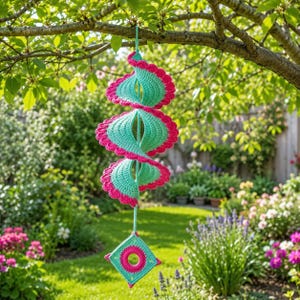 May include: A spiral-shaped hanging decoration made of crocheted yarn in alternating turquoise and bright pink colours. The structure features a series of curved, scalloped-edge segments and terminates in a square-shaped base with a central circular cutout.