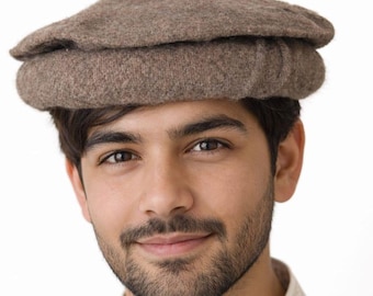 May include: A brown Pakol hat, a traditional, round, and folded hat, is featured. The hat is made of wool or sheep's wool and is worn on the head. The person is wearing a white shirt with a detailed collar.